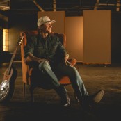 Cooper Alan sat on a chair with a guitar beside him